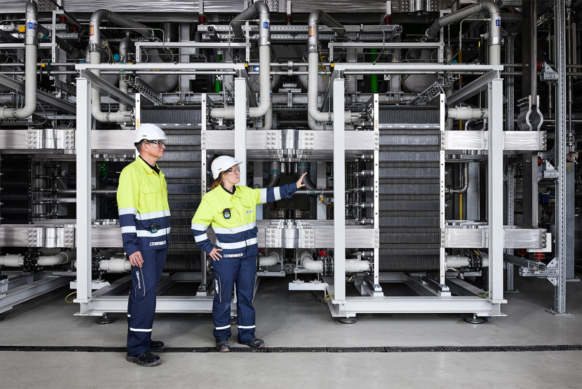 Workers examining a large proton exchange membrane (PEM) electrolyzer stack used for green hydrogen production.