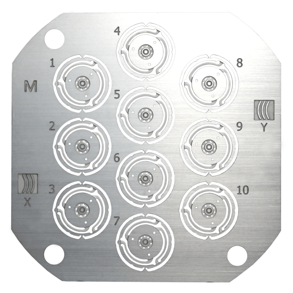 Stainless steel etched button spring plate with numbered circular spring mechanisms arranged in a 1–10 grid, showing precision-machined components used in mechanical assemblies.